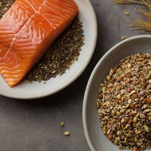 Fontes de Ômega 3, incluindo filé de salmão, sementes de chia, sementes de linhaça e nozes, dispostas sobre a mesa em um contexto de receita fitness.